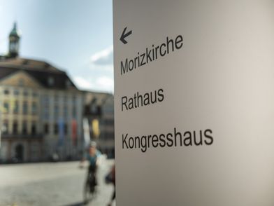 Wegweiser auf dem Marktplatz in Coburg mit dem Rathaus im Hintergrund