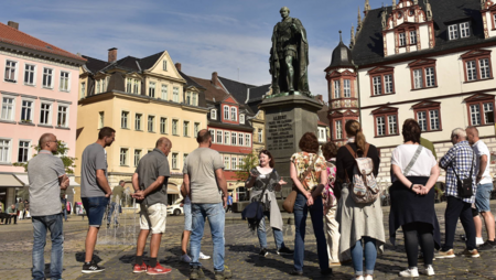 Eine Gästeführerin erzählt einer Reisegruppe mehr über den historischen Marktplatz in Coburg.