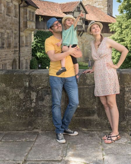 Eine Familie steht an einer Mauer auf der veste Coburg und ein Elternteil hat das Kind auf dem Arm, welches nach oben zeigt.