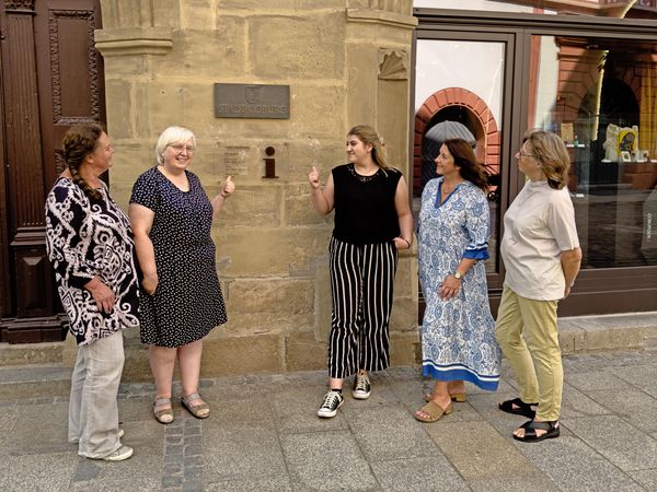 Mitarbeiterinnen der Tourist-Information in Coburg zeigen auf das Schild am Eingang.