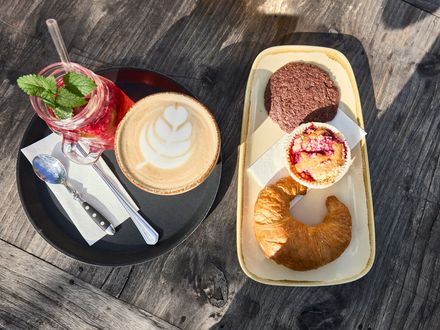 Ein Kaffeegetränk mit Milchschaum, ein kaltes Getränk und süßes Gebäck machen Appetit. 