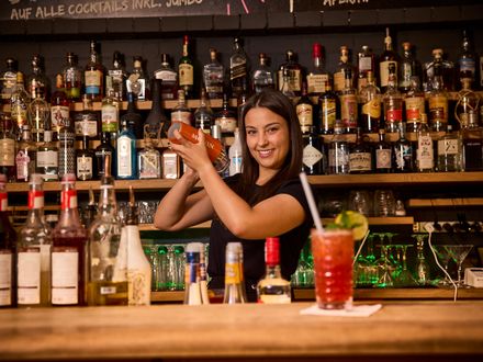 Eine strahlende Bartender zaubert in einer gut ausgestatteten Bar leckere Cocktails.